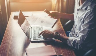 Businessman hands using cell phone with laptop at office desk.