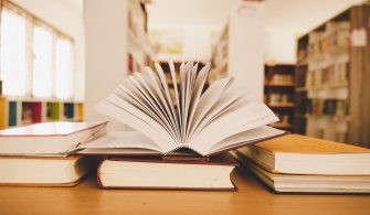 Book in library with old open textbook, stack piles of literatur