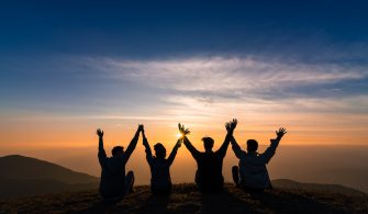 silhouette of friends shake hands up and sitting together in sun