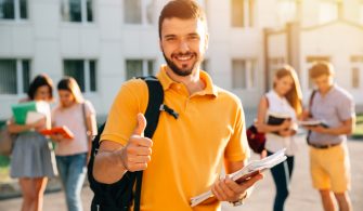 Young attractive smiling student showing thumb up outdoors on campus at the university