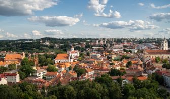 Vilnius city surrounded by buildings and greenery under sunlight and a cloudy sky in Lithuania
