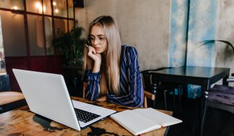 Pensive long-haired girl in glasses looking at laptop screen. Wi