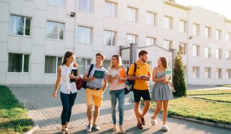 Five friendly students are walking after they passed test outside the college building and discuss the project