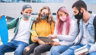 multiracial-teenage-friends-wear-face-mask-sitting-tha-bench-outside-school-new-normal-lifestyle-concept-with-young-students-studing-together-near-campus-outdoors_296748-4
