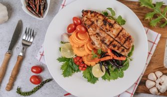 Chicken Steak with Lemon, Tomato, Chili, and Carrot on White Pla
