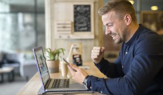 Happy freelancer with tablet and laptop computer in coffee shop.