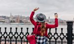 Portrait from back of stylish young woman in checkered shirt waving hands on city background. Excited long-haired female model enjoyng river views in cold day..